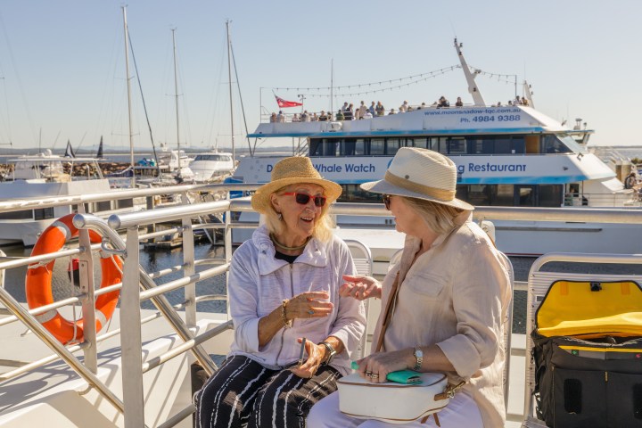 Two women in hats chatting on a boat with another tour boat in the background.