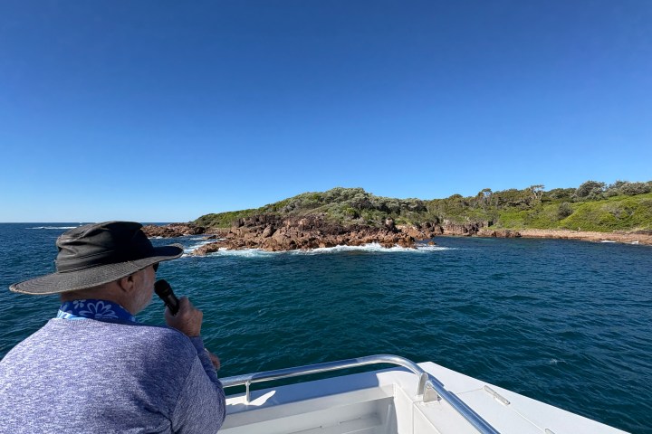 Person on boat looking at rocky island and ocean under clear blue sky.