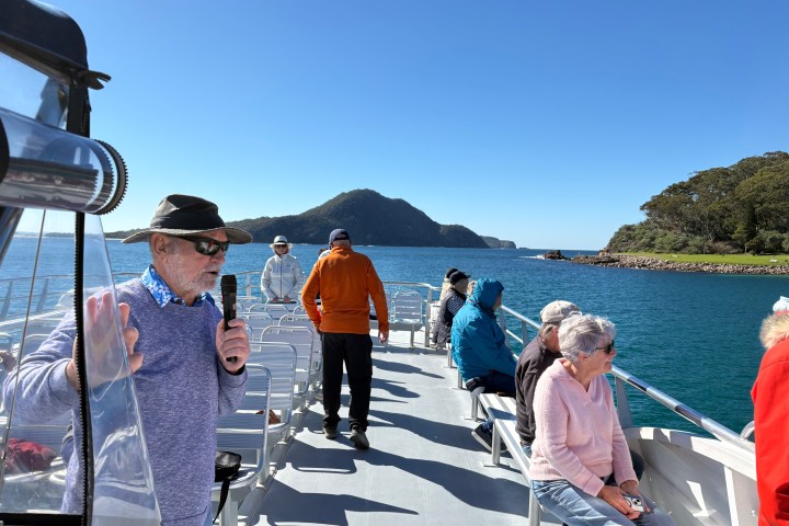 People on a boat with a scenic mountain and ocean view on a sunny day.