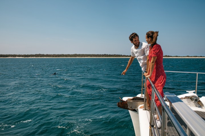 Man and woman on a boat look at the ocean and distant land.
