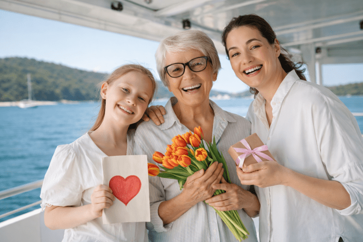 Three women smiling on a boat, holding tulips, a gift, and a heart card.