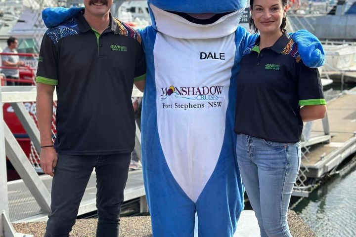 Two people pose with a blue whale mascot on a dock.