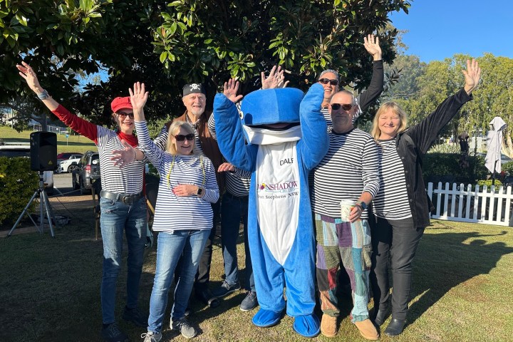Group of people in striped shirts posing with dolphin mascot outdoors.