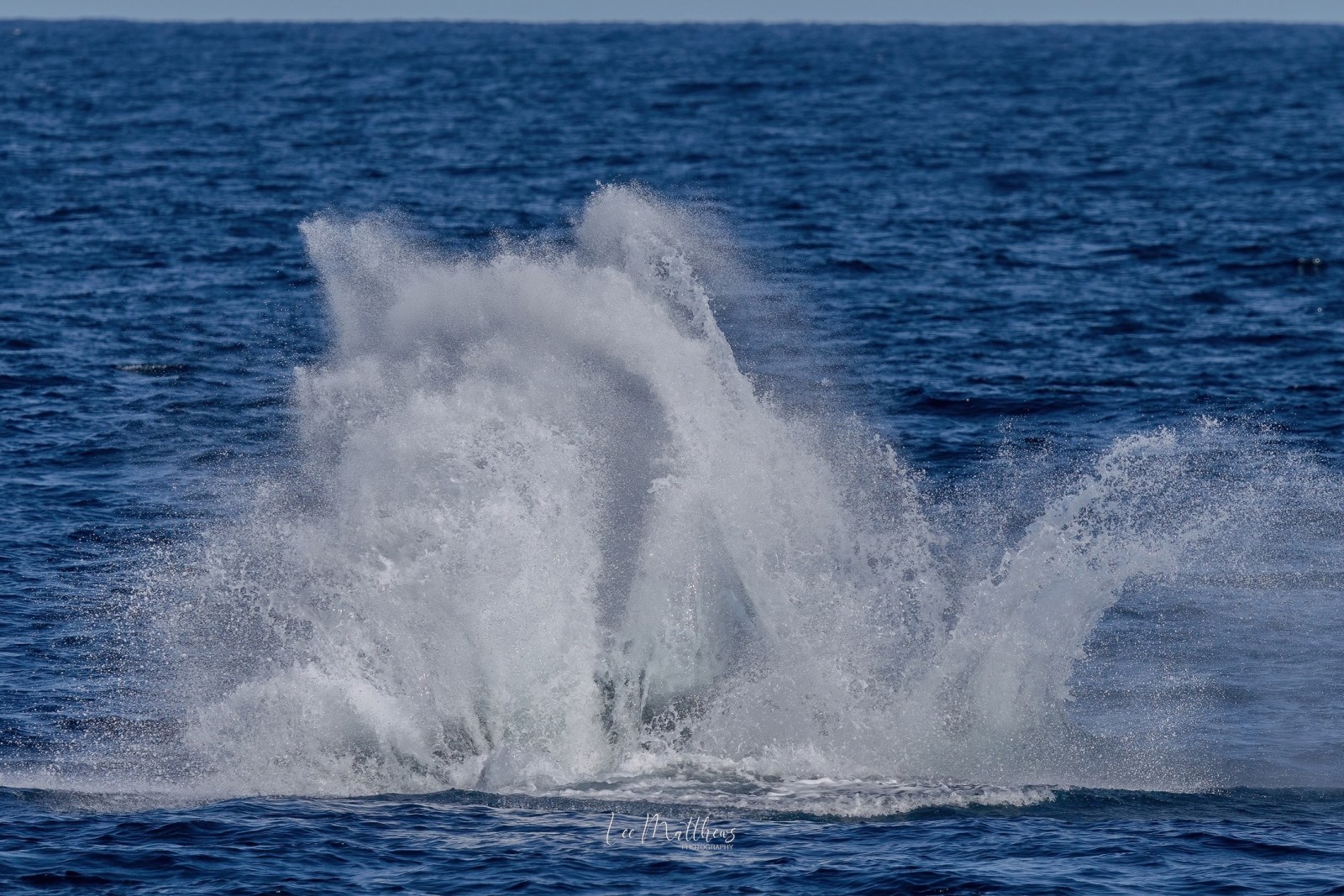 A large splash in the ocean under a clear blue sky.