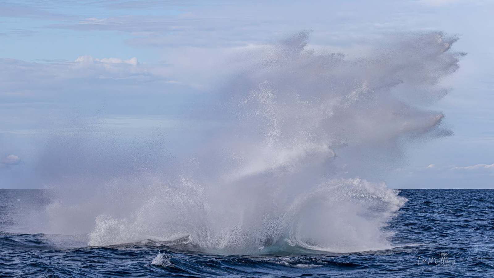 Large splash in the ocean under a cloudy sky.