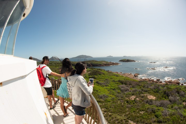 People on a viewing deck overlooking the ocean and islands on a sunny day.