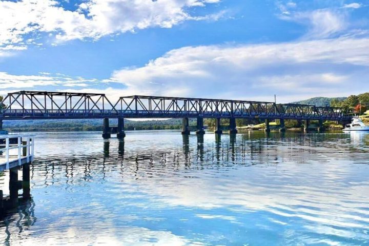Steel bridge over a calm river under a partly cloudy sky.