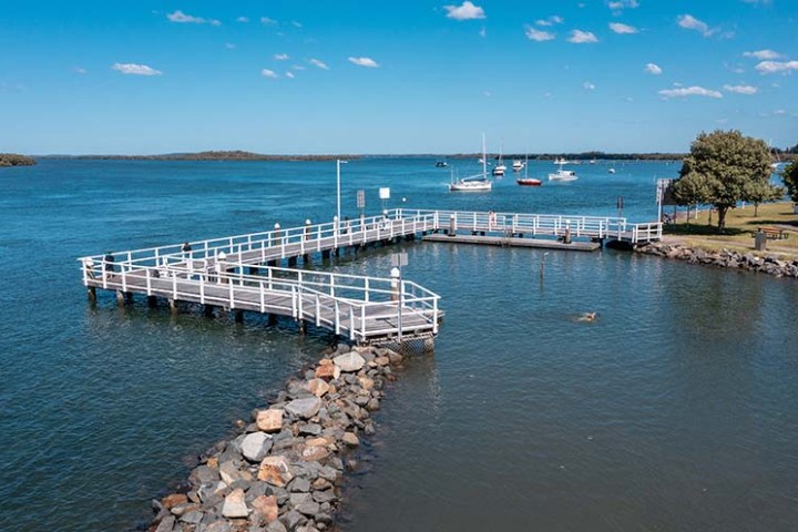 Scenic view of a pier extending into a calm lake with boats and a clear blue sky.