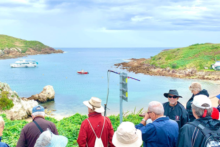 Group of tourists overlooking a scenic bay with boats and green hills.